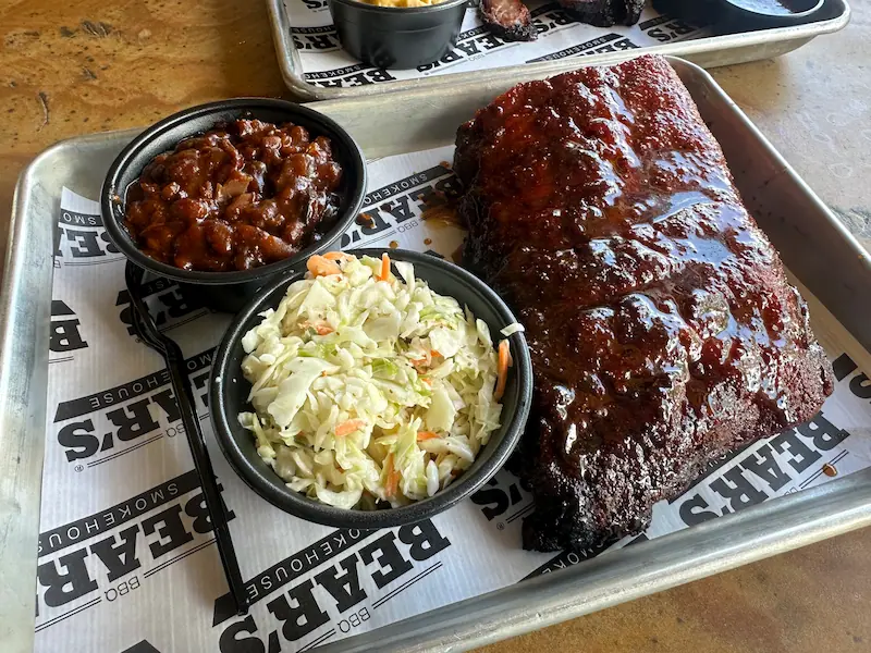 A tray of slow-smoked ribs with glazed bark, creamy coleslaw, and BBQ beans from Bear's Smokehouse in Asheville, NC.